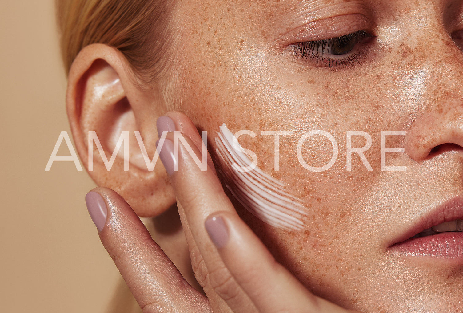 Close up highly detailed shot of a young woman applying cream on her freckled skin. Cropped shot of woman applying moisturizer on cheek with fingers.