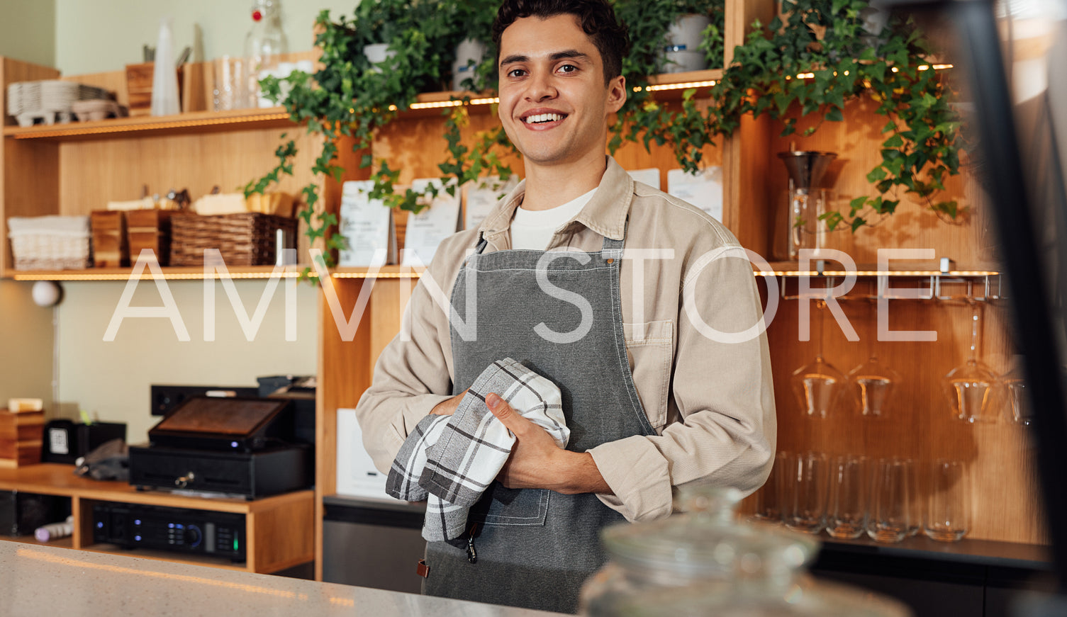 Smiling bartender in apron wiping hands with towel at counter