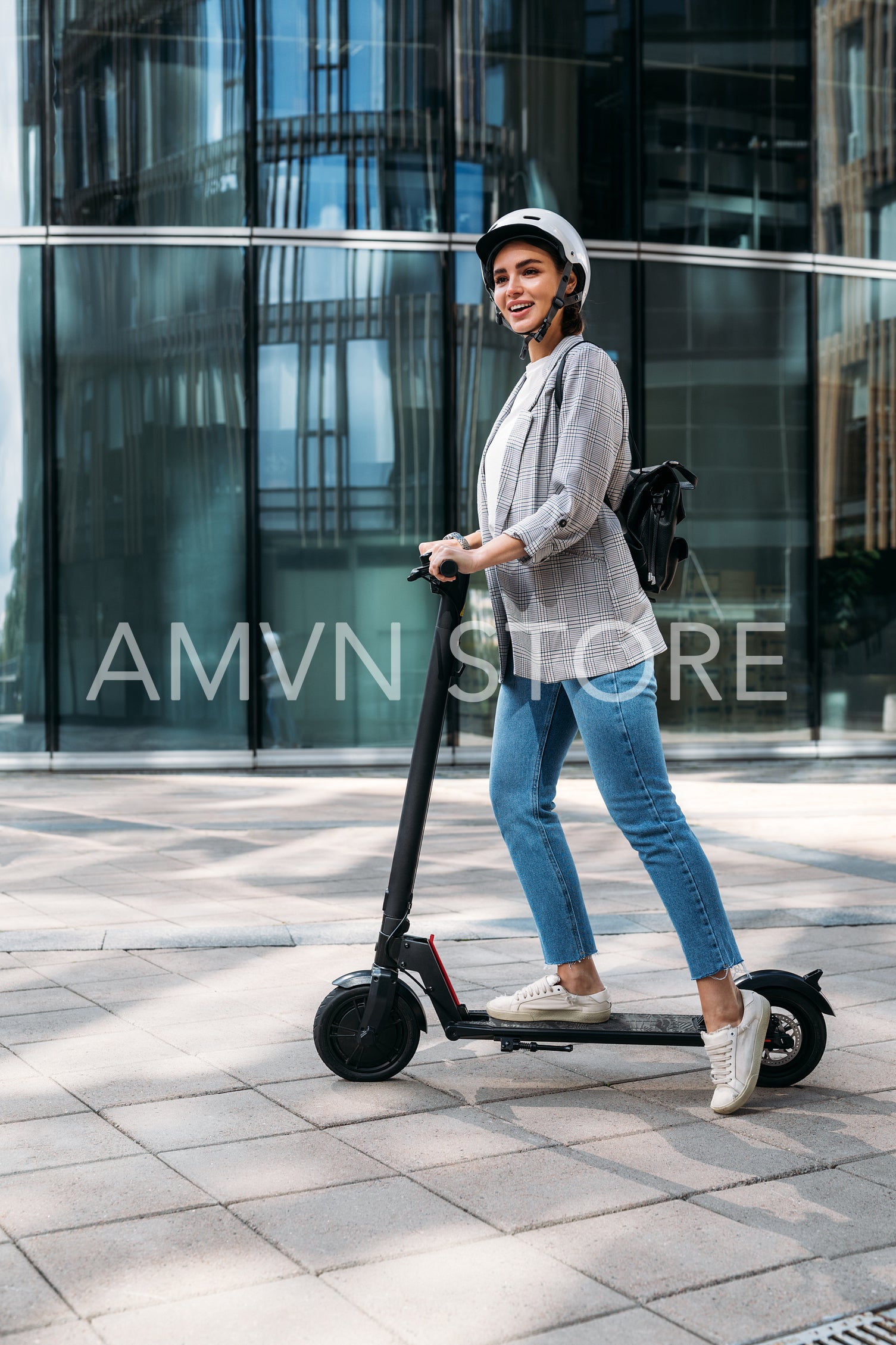 Young happy woman in casuals driving electric push scooter. Businesswoman in cycling helmet standing on e-scooter.