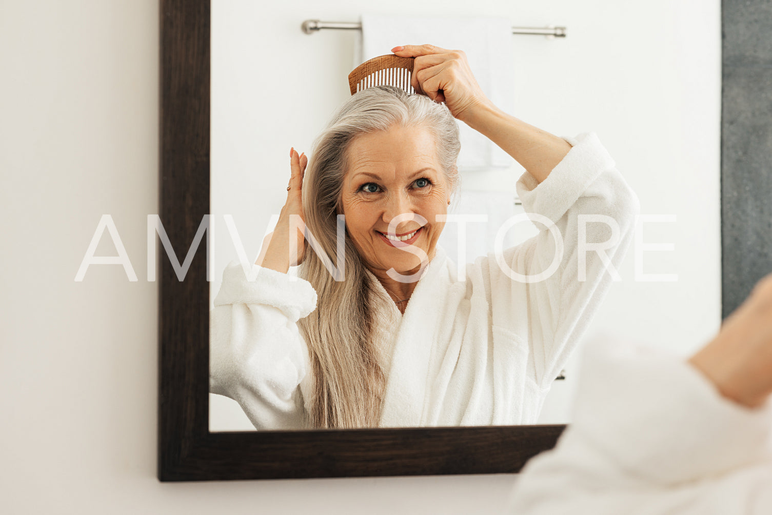 Smiling senior woman combing her grey hair in front of a bathroom mirror