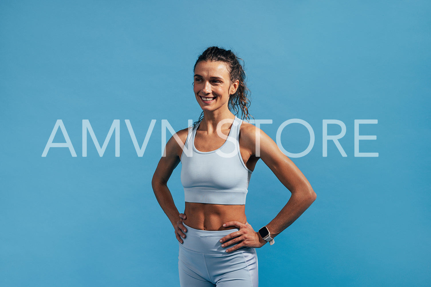 Cheerful woman in fitness wear with hands on her waist on blue background