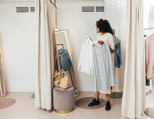 Young woman choosing clothes while standing in fitting room in a boutique