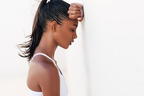 Female with drops of sweat on her face relaxing a white wall with closed eyes