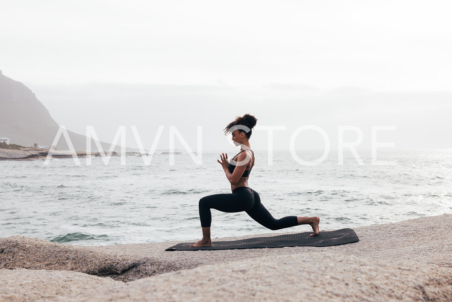 Woman in fitness wear practicing yoga on a mat at seashore