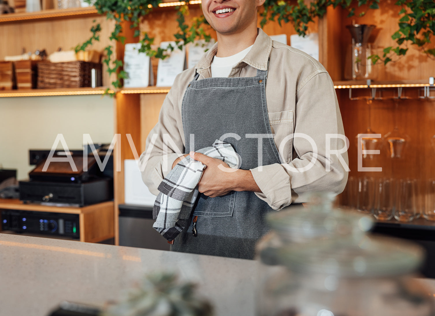 Cropped of an unrecognizable bartender in apron wiping his hands with towel while standing at bar counter