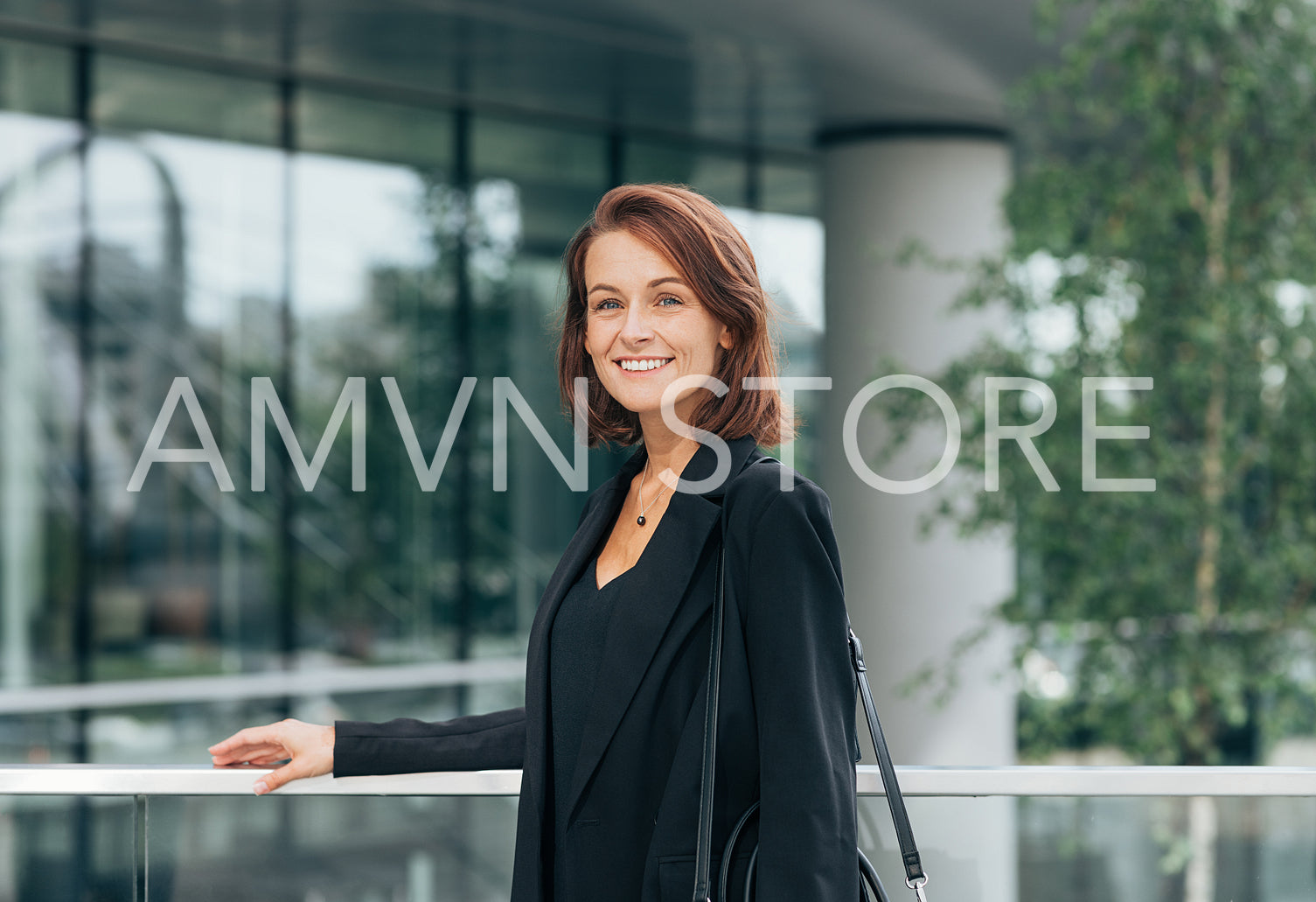 Portrait of a cheerful middle-aged female in black formal clothes. Businesswoman with ginger hair at railing outdoors.