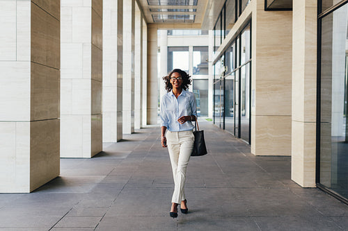 Young smiling woman walking on city street to office carrying her bag