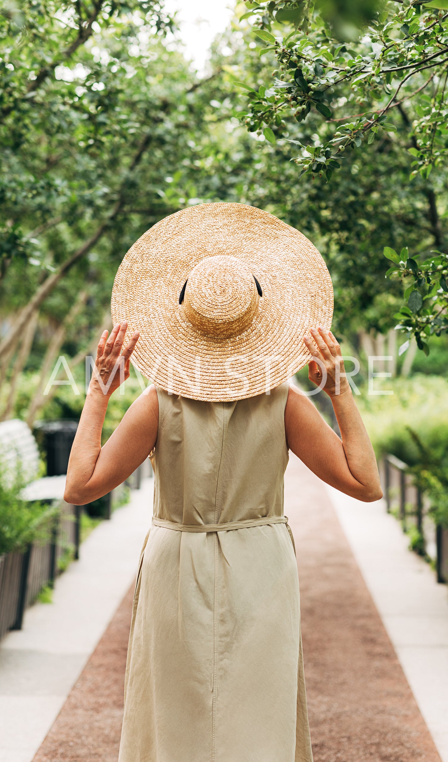 Back view of an unrecognizable senior woman in a long dress holding a straw hat