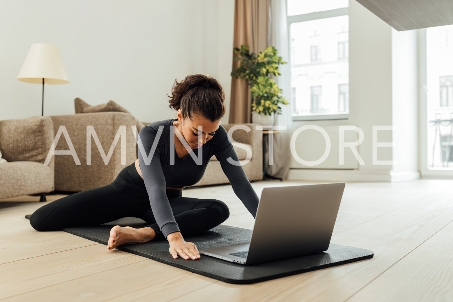 Young middle east woman doing yoga exercise at home. Female in sportswear sitting on mat and stretching her legs in front of a laptop.	