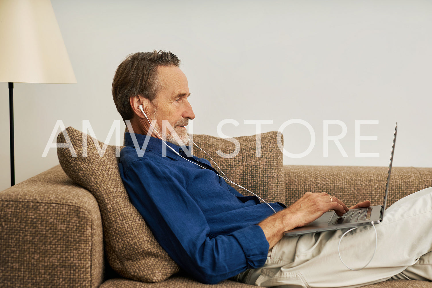 Side view of a handsome senior man lying on sofa typing on laptop