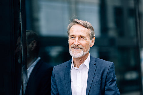 Smiling businessman standing outdoors at office building and looking away