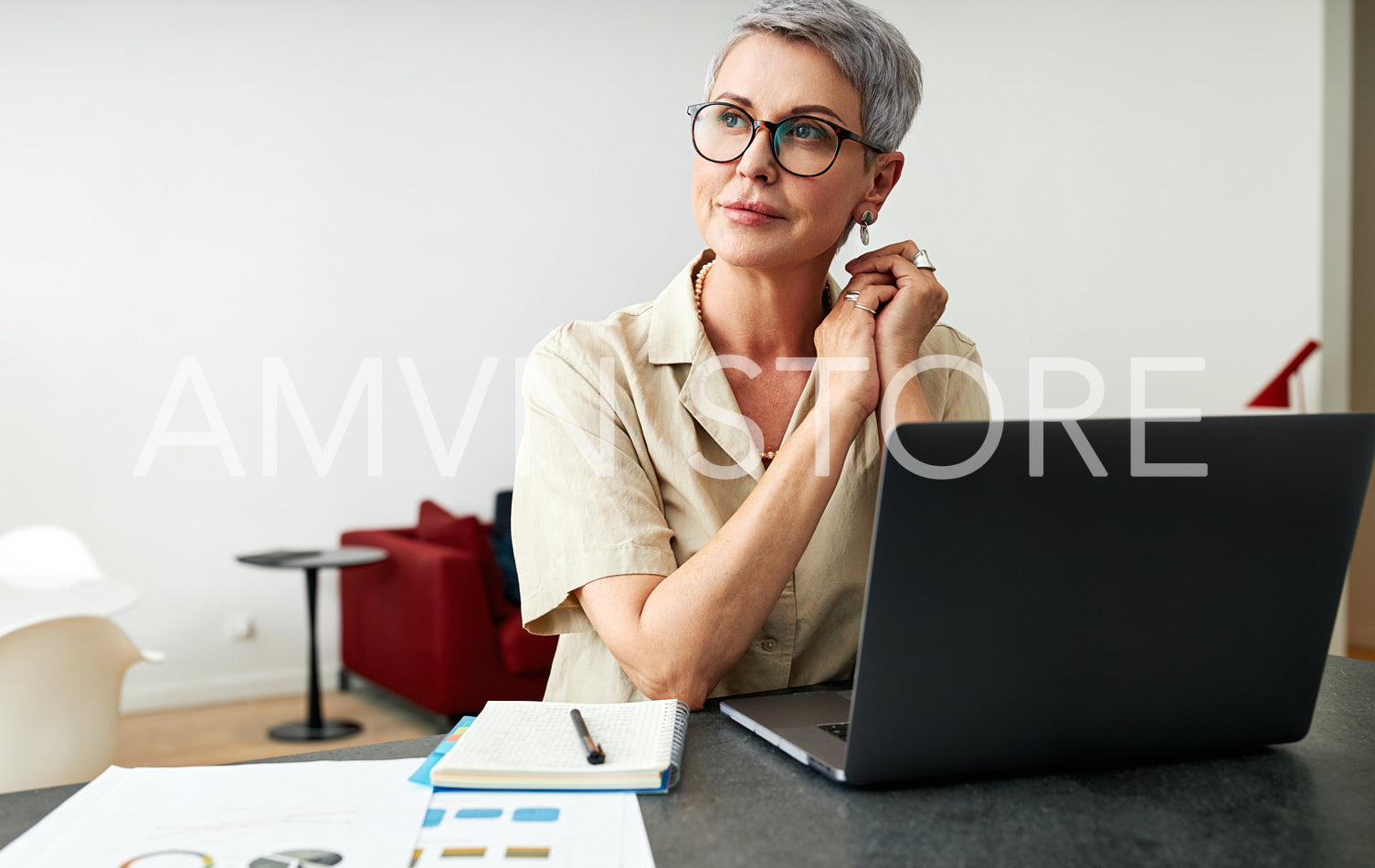 Thoughtful mature woman wearing eyeglasses sitting at a desk at home looking away	