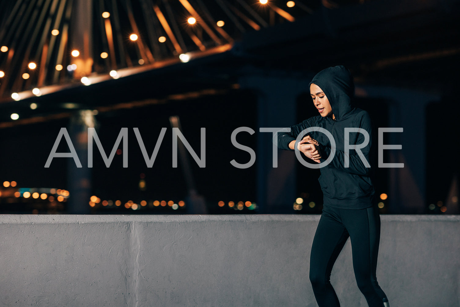 Young sportswoman looking at smartwatch while running at night outdoors