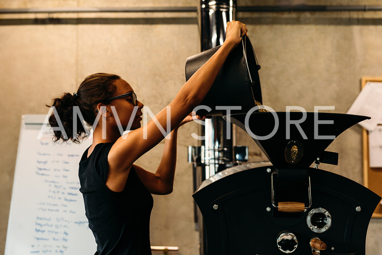 Young businesswoman pouring coffee beans into a roasting machine at her coffee shop.	