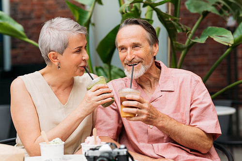 Happy aged couple drinking cocktails in an outdoor cafe. Smiling mature couple enjoying drinks outdoors.