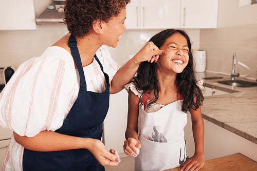 Grandmother and granddaughter are playing with flour in kitchen. Granny touching granddaughter's face with flour covered finger.