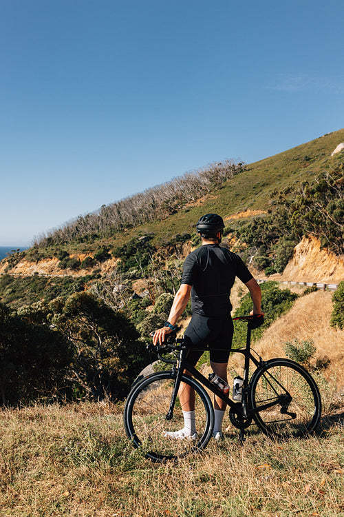 Professional cyclist in black sportswear leaning his bike looking at the view