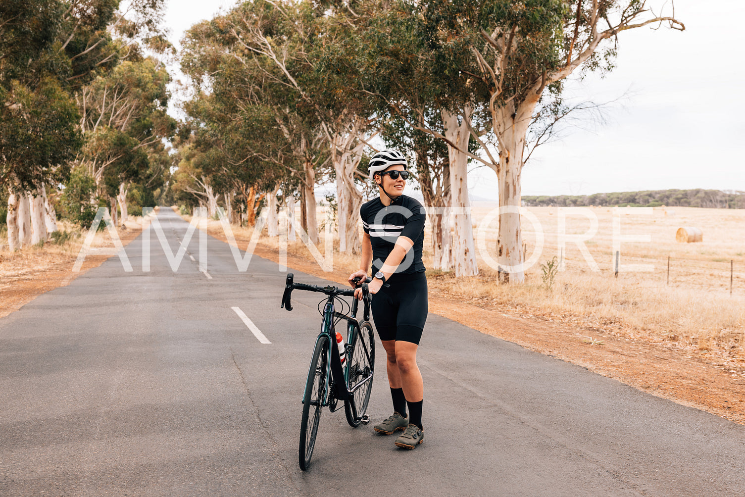 Professional woman cyclist standing with her bike on the centre of the countryside road