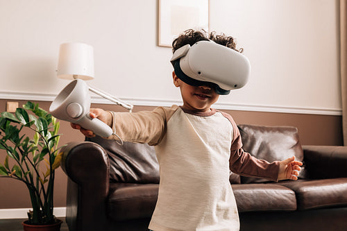 Little boy wearing VR glasses and holding a controller while standing in living room