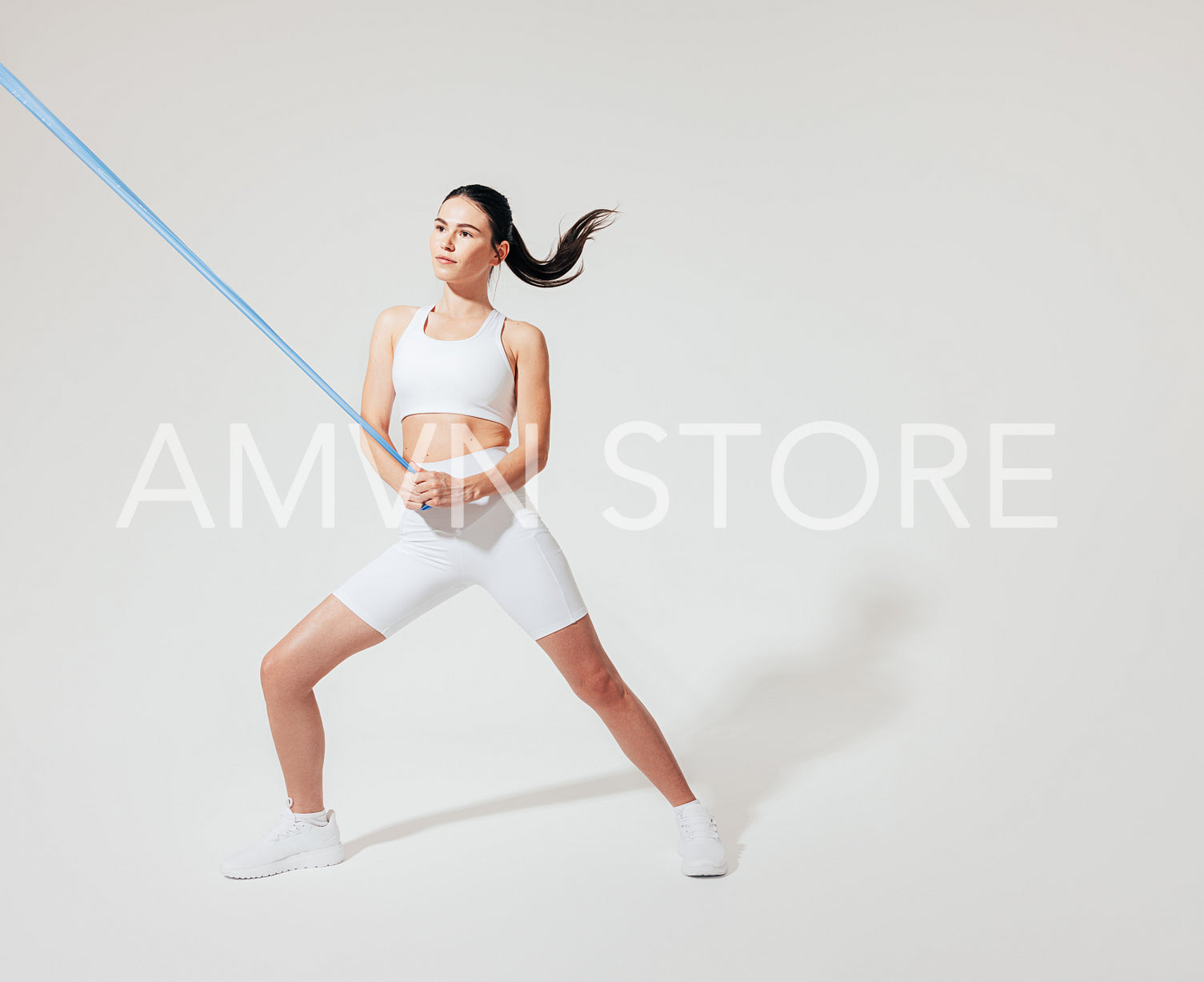 Young slim woman in white fitness wear practicing on a white backdrop with a resistance band