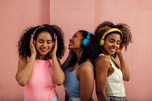 Group of female friends in casuals wearing headphones standing t