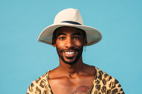 Smiling guy in straw hat looking at camera while standing in studio over blue background