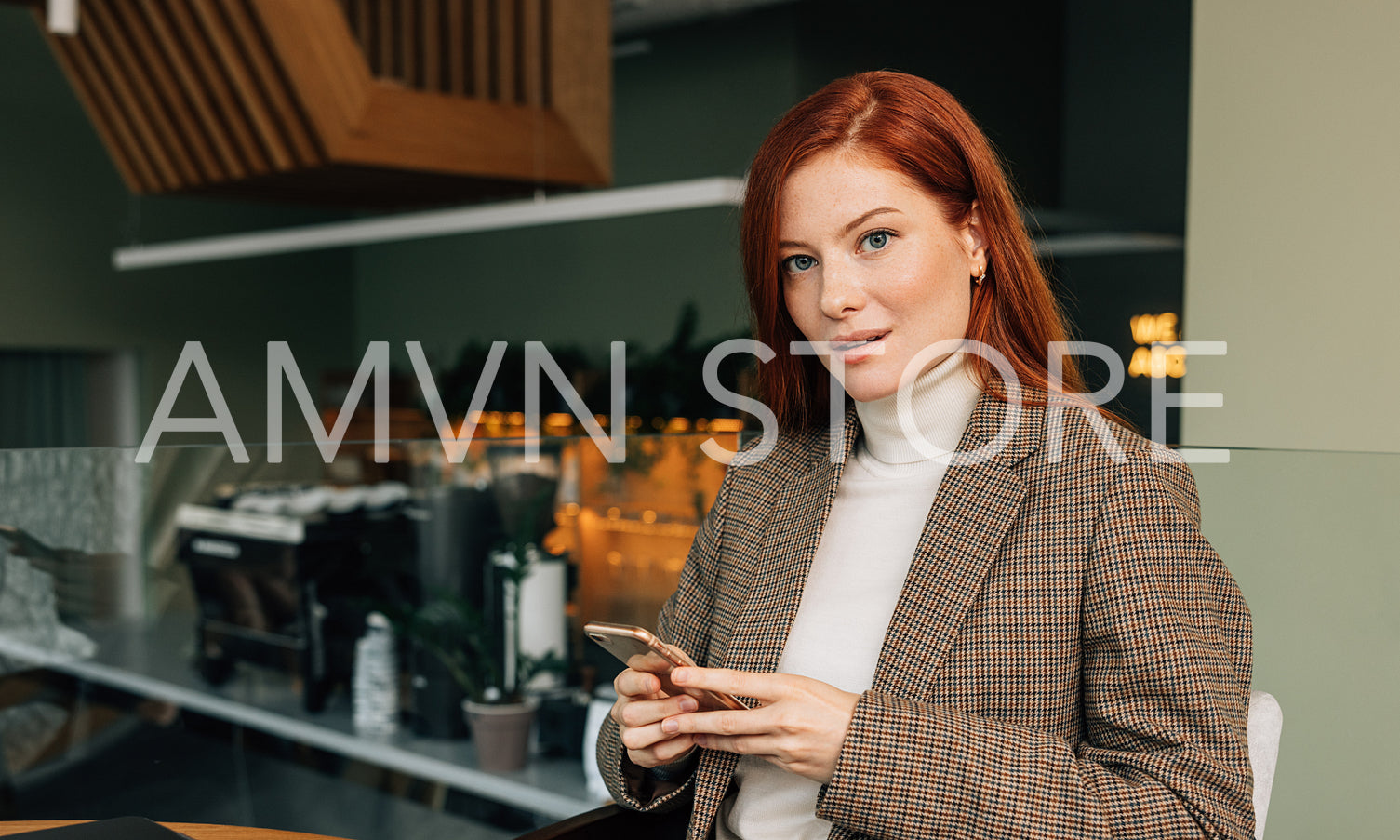 Portrait of a young businesswoman with ginger hair in a cafe. Female in formal wear holding a smartphone looking at camera.