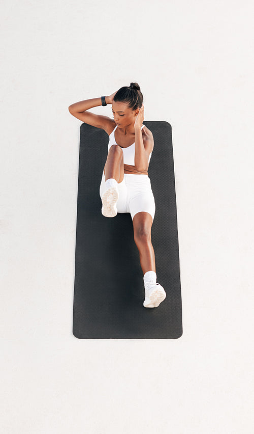 High angle of a fit woman doing abs exercises. Full length of a young female on a mat outdoors.