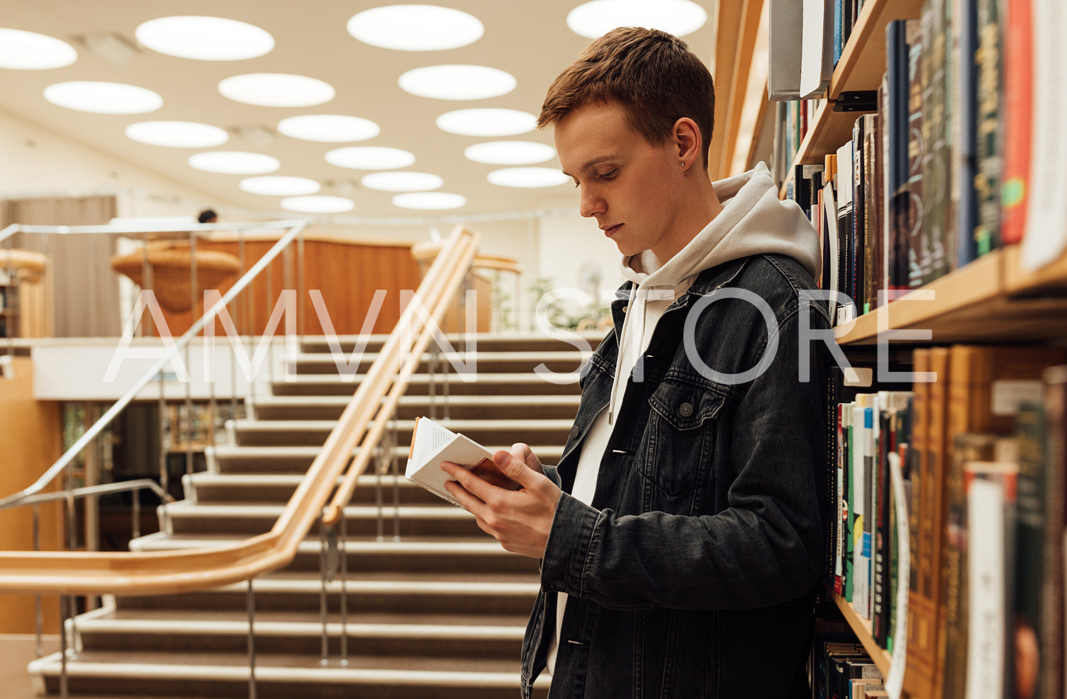 Side view of a male student standing at bookshelf and reading