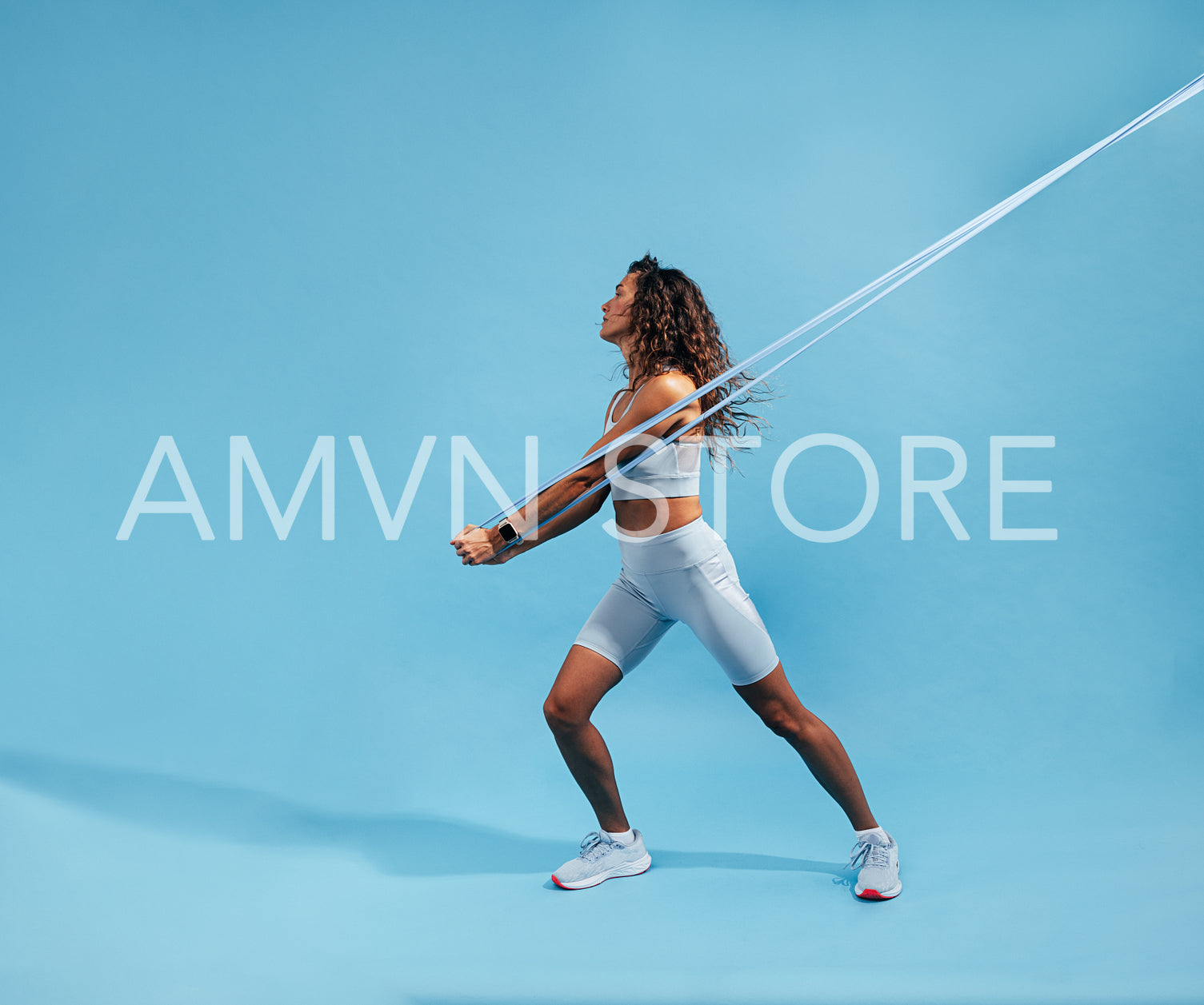 Female working out with elastic band on blue background. Slim athletic woman working on core strength with resistance band. 