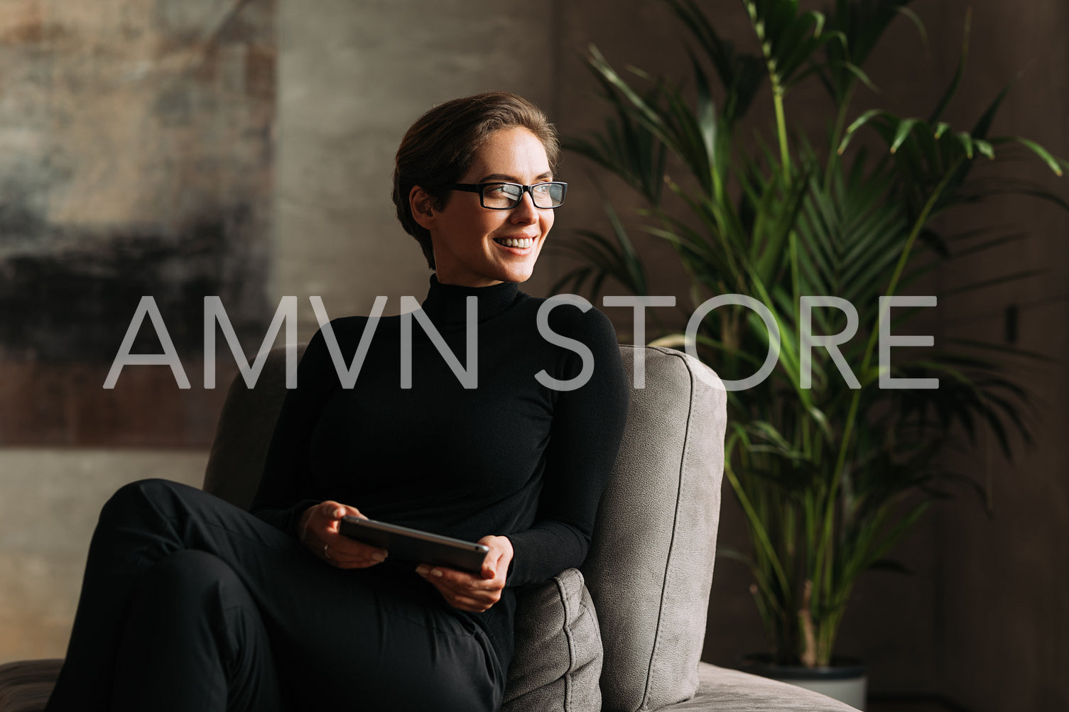 Smiling businesswoman looking away while sitting indoors holding a digital tablet