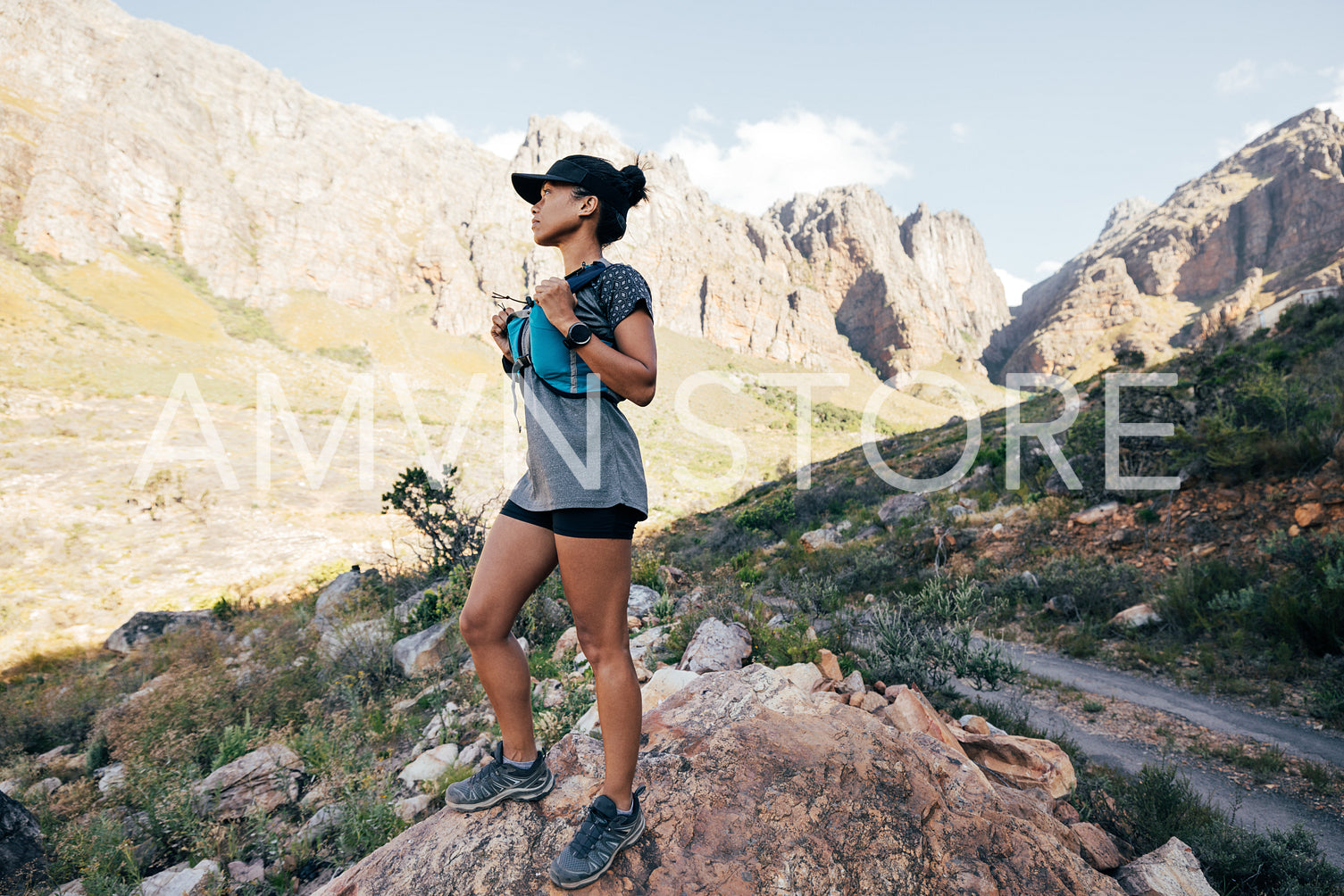 Side view of trail runner in sports wear standing in valley. Young female in fitness attire in wild terrain.