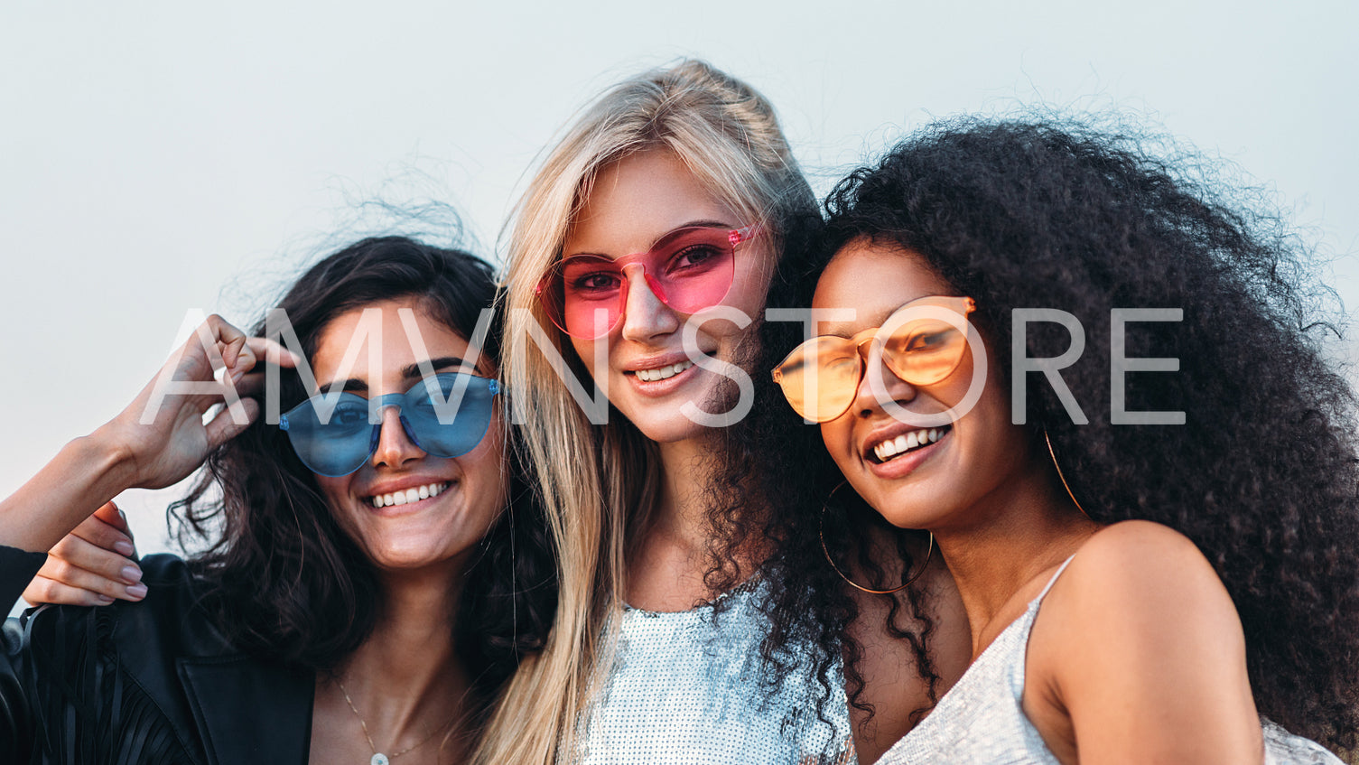 Three happy women wearing sunglasses hugging at evening outdoors	