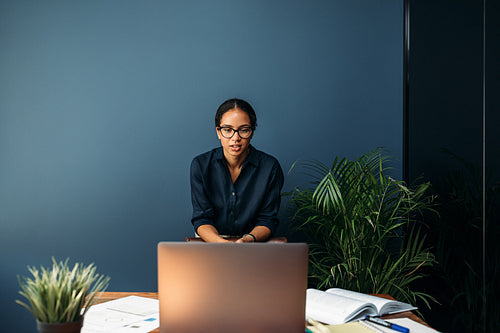 Young businesswoman standing at the desk in home and having a video chat over her laptop