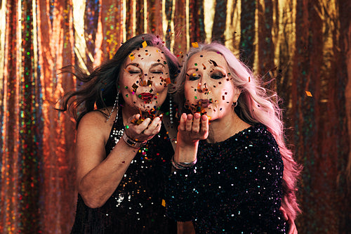 Two senior women in black dresses blowing confetti off their han