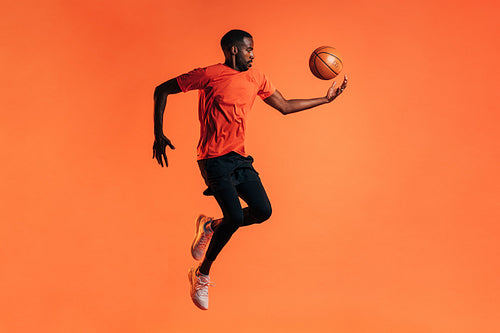 Side view of young male jumping and throwing up a basket ball in studio