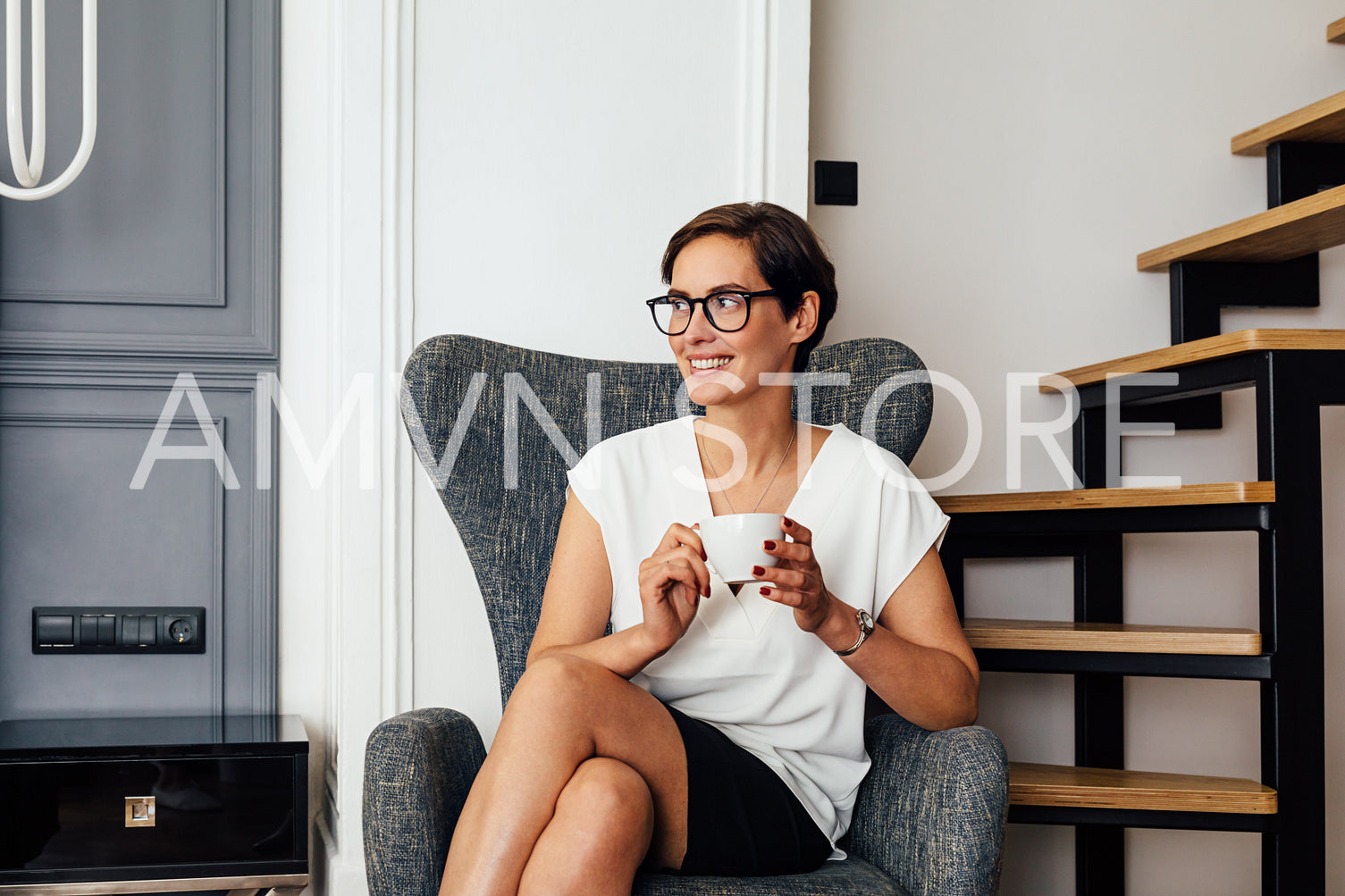 Beautiful smiling woman holding a cup of coffee and looking away while sitting in hotel room	