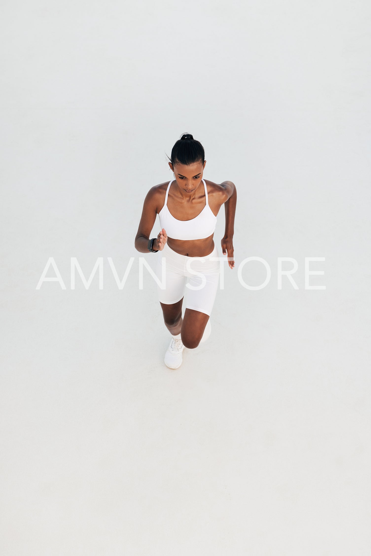 Shot from above of a young woman running in a white outdoor studio. High angle of a slim female sprinting.