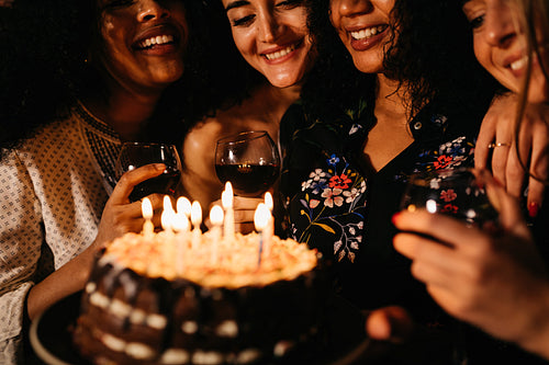 Happy girlfriends celebrating a birthday, holding a cake with lit candles