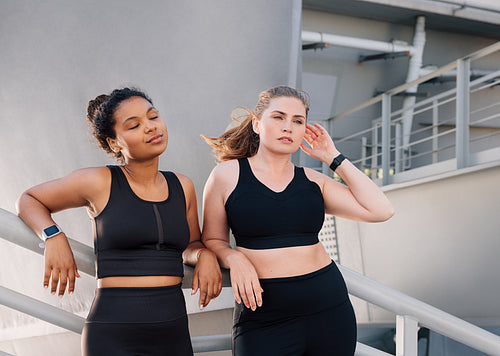 Two young females wearing fitness attire with the same color relax after a workout. Plus-size women relaxing outdoors during workout.