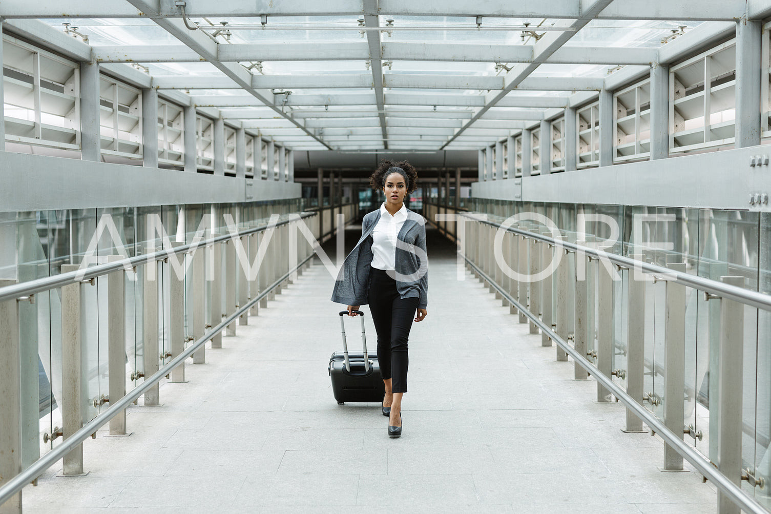 Woman traveller pulling suitcase in airport corridor, front view	