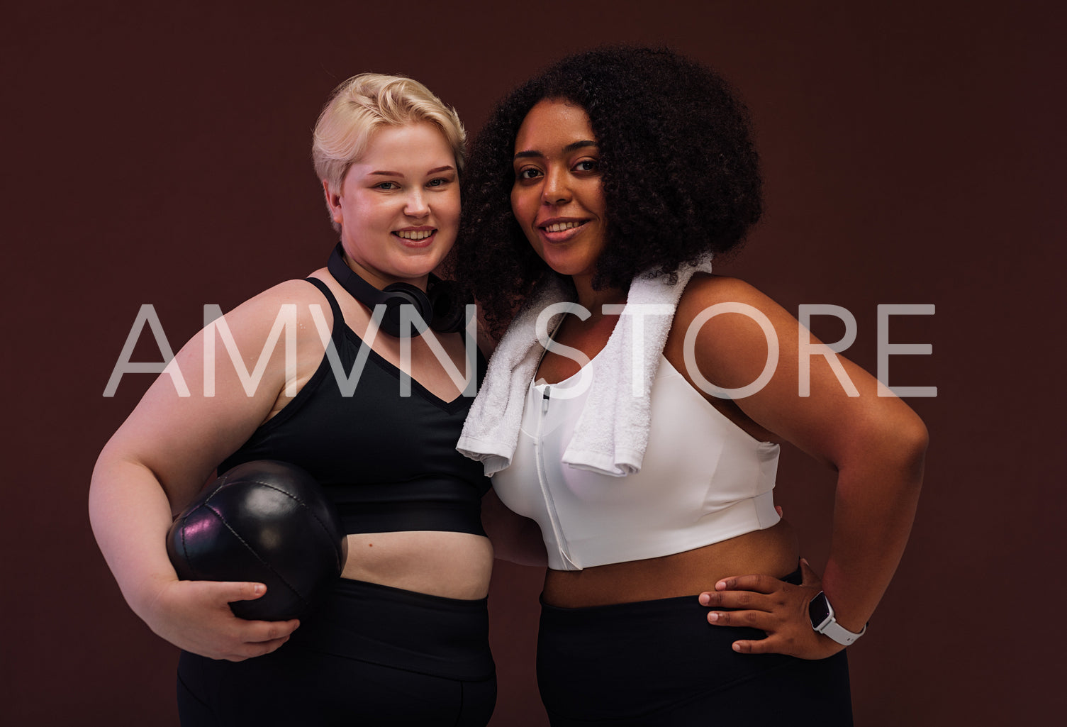 Two plus size females with fitness accessories standing together on brown background