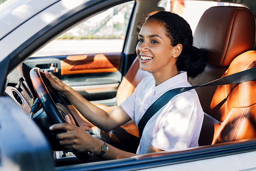 Smiling woman driving looking out a car window. Happy woman holding a steering wheel in the vehicle.