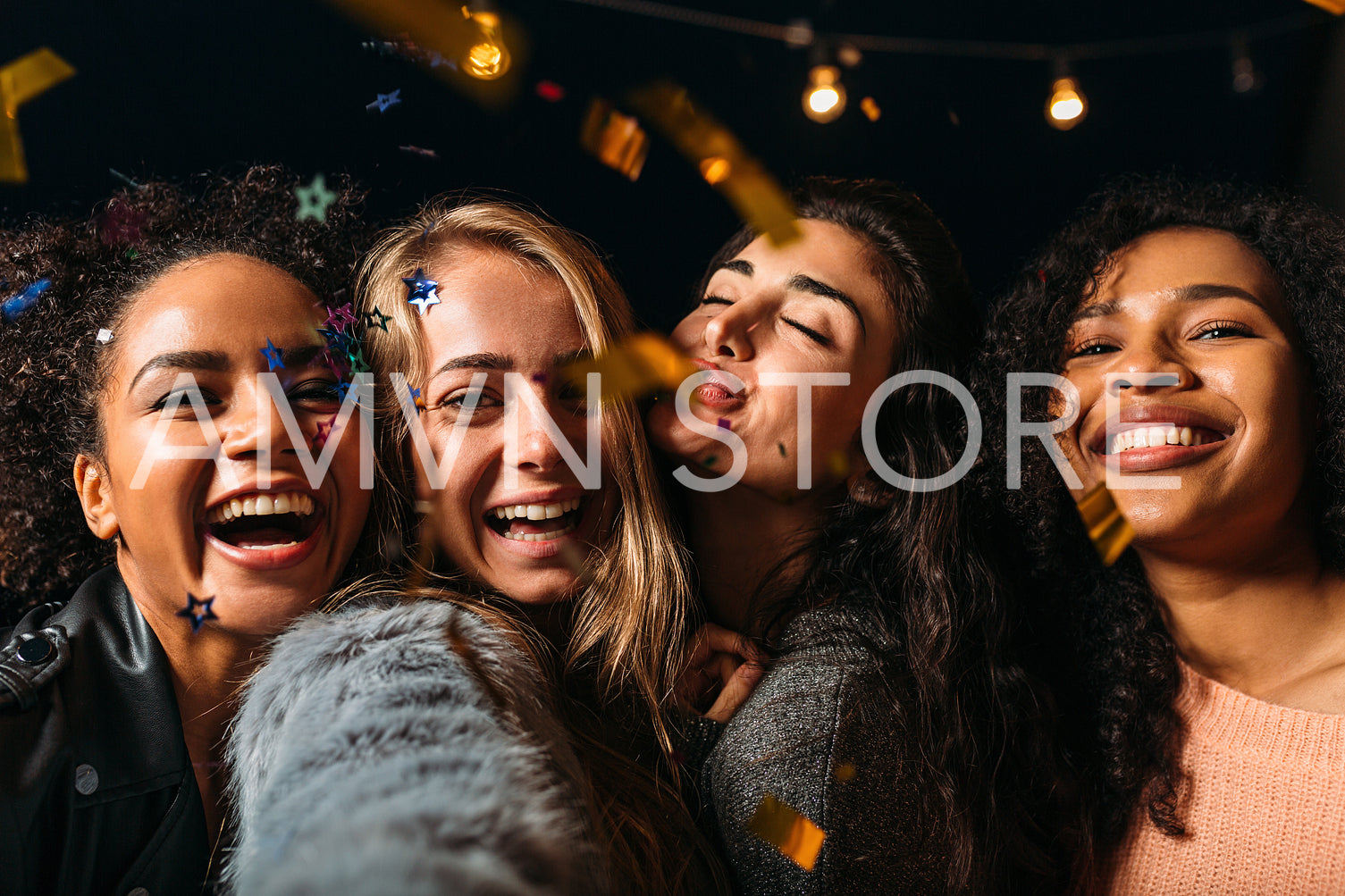 Four laughing girls taking selfie under confetti at night