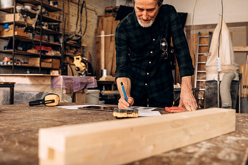 Male carpenter planning his work. Senior man making notes in carpentry.