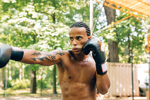 Sweated bare-chested sportsman with boxing gloves exercising outdoors