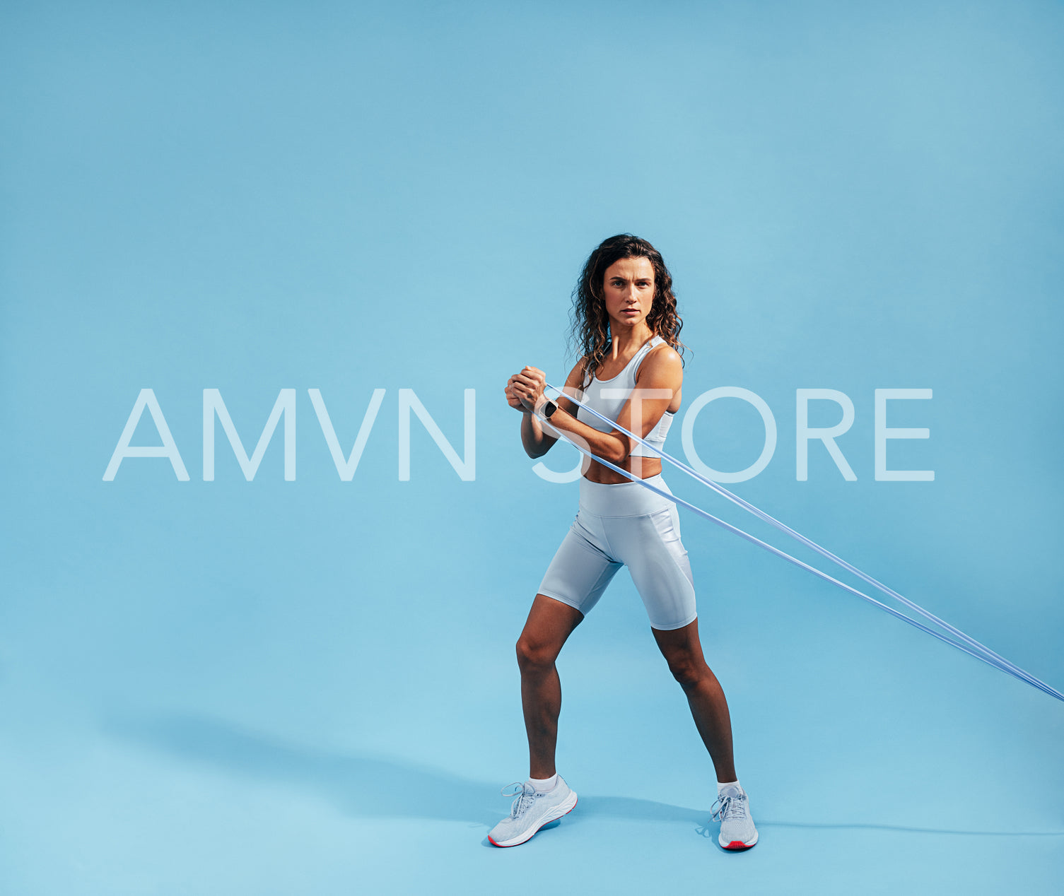 Slim athletic woman working out on blue background. Fit woman looking at camera using stretch band.