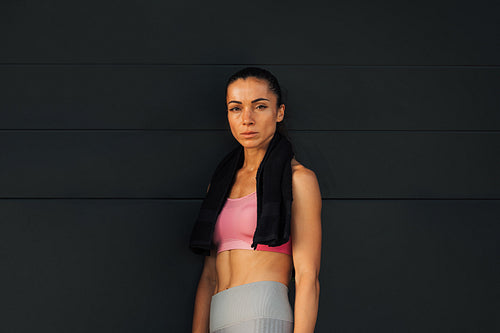 Woman athlete standing at black wall and looking at camera