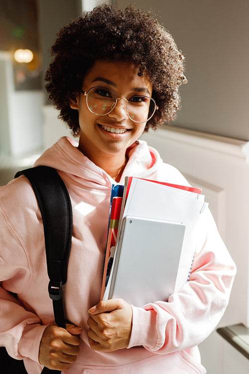 Young smiling student with books and digital tablet standing in college corridor