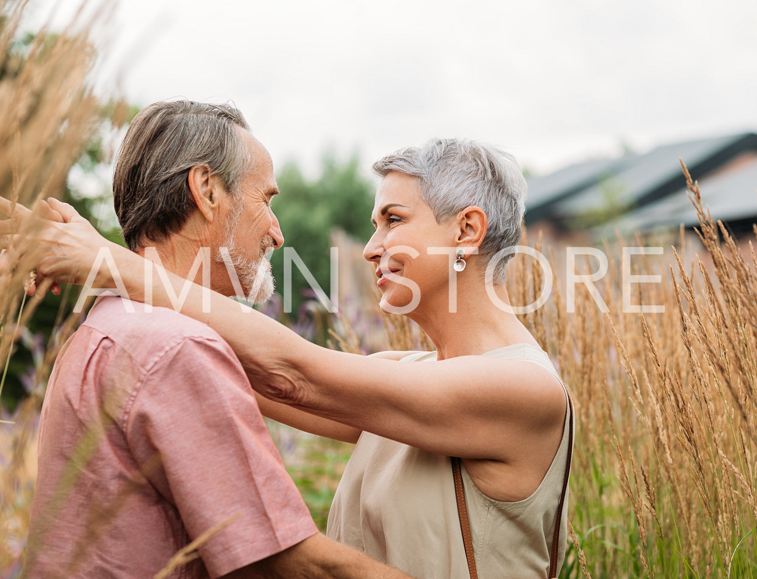 Aged people hugging and looking at each other while standing on a wheat field.